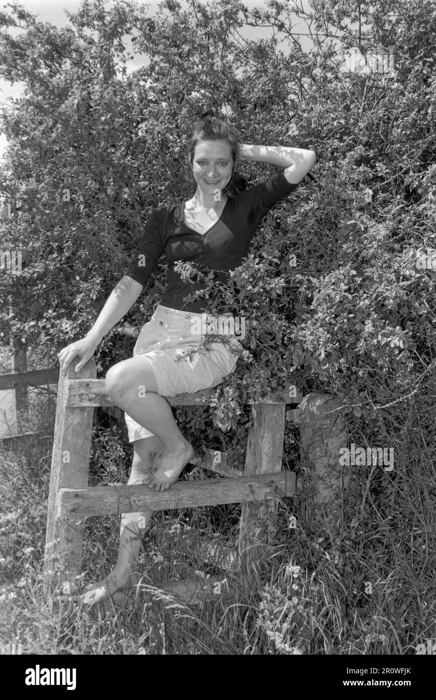 Junge, schlanke, hübsche, dunkle weibliche Haare, die auf einem Holzzaun posierten, während des Country Walk 1990er england uk Stockfoto