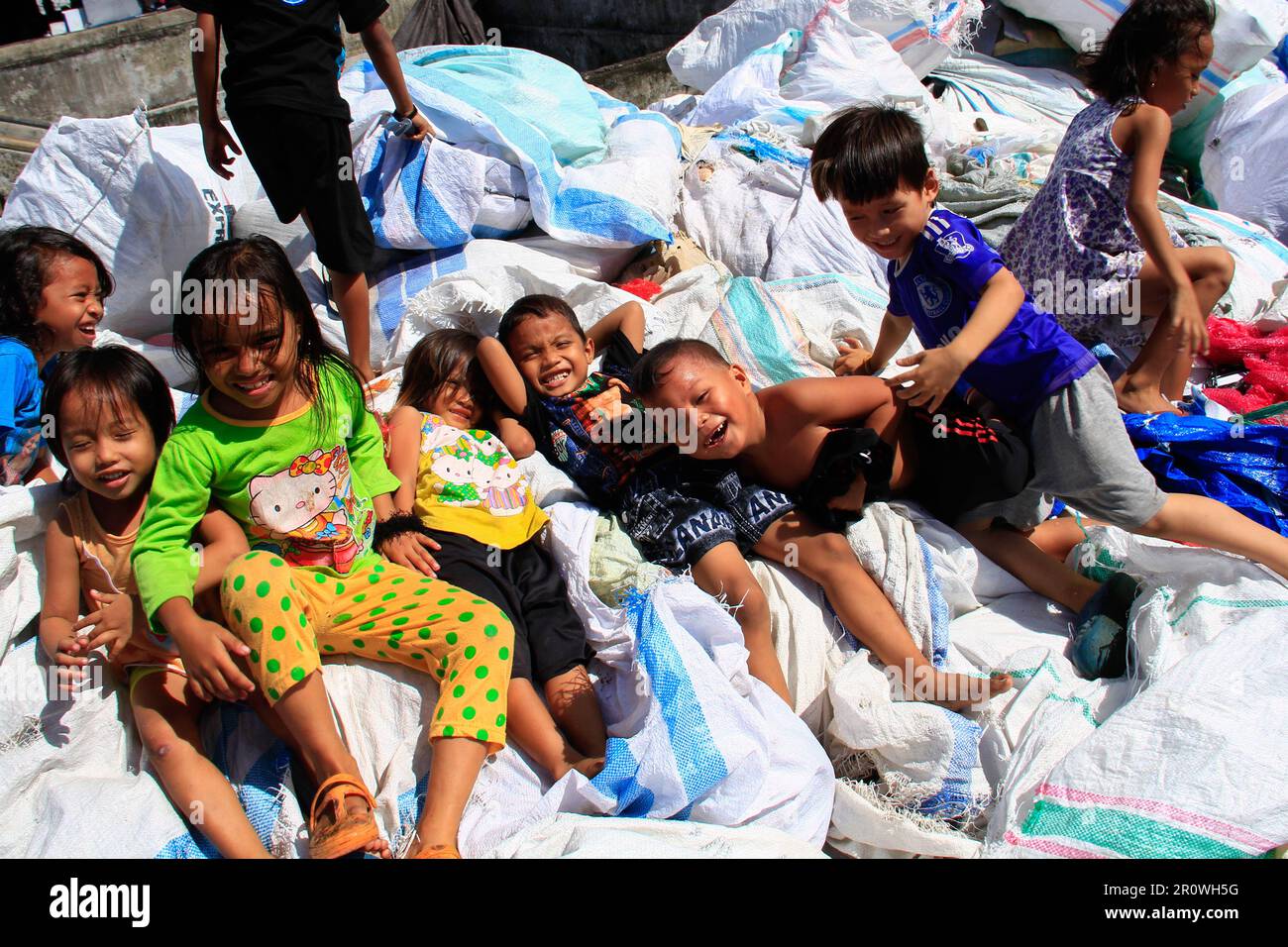 Kinder, die in Müllsäcken spielen und in der heißen Sonne Platz suchen. Stockfoto