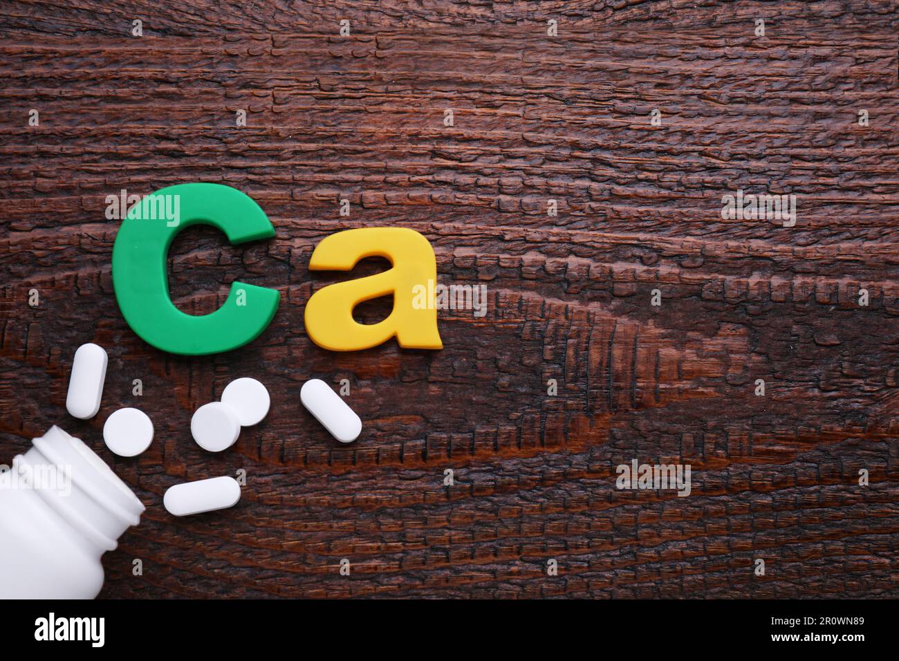 Papiersymbol Ca (Calcium), medizinische Flasche und Pillen auf Holztisch, Draufsicht. Platz für Text Stockfoto