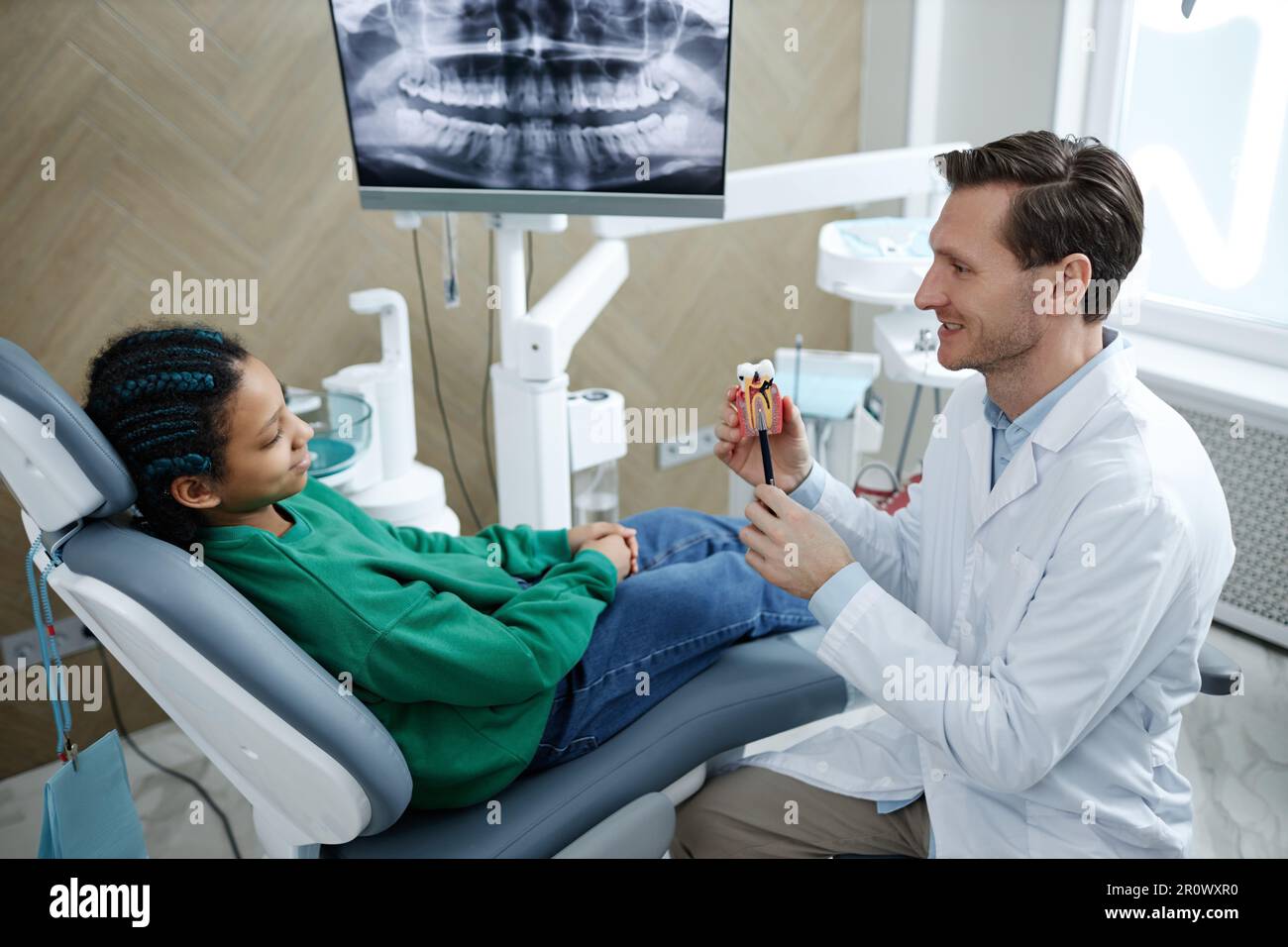 Lächelndes männliches Zahnarzthalter-Zahnmodell während der Beratung eines kindlichen Patienten in der Zahnklinik, Kopierraum Stockfoto