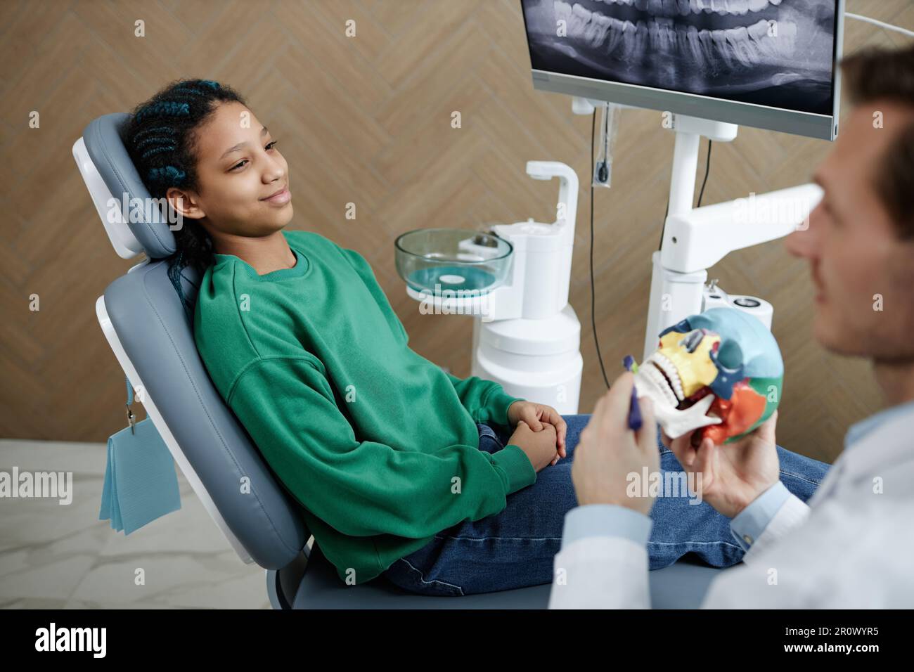 Das Porträt eines schwarzen Teenagers in der Zahnklinik, sitzt im Stuhl und hört Zahnarzt in der Sprechstunde Stockfoto