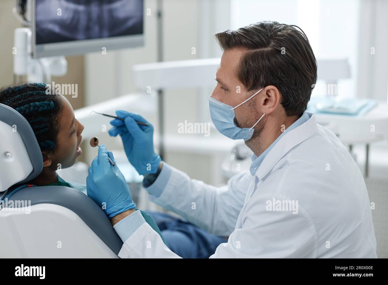 Seitenansicht des maskierten männlichen Zahnarztes bei der Arbeit mit einem kindlichen Patienten in der Klinik Stockfoto