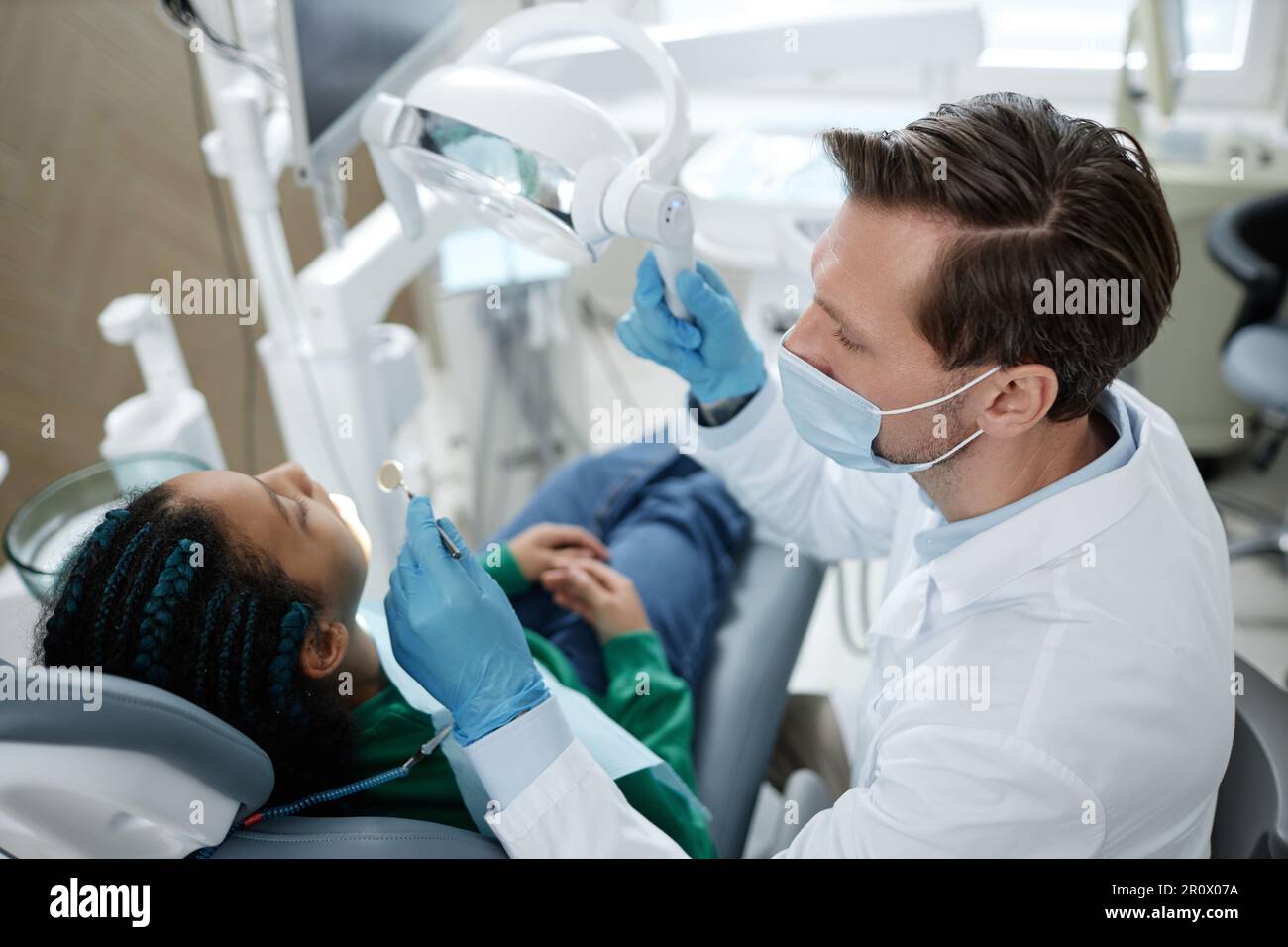 Hochwinkelblick beim männlichen Zahnarzt mit Maske während der Arbeit mit dem Kind in der Zahnklinik Stockfoto