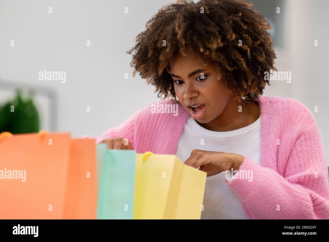 Eine überraschte schwarze Frau, die in bunte Einkaufstüten schaut Stockfoto