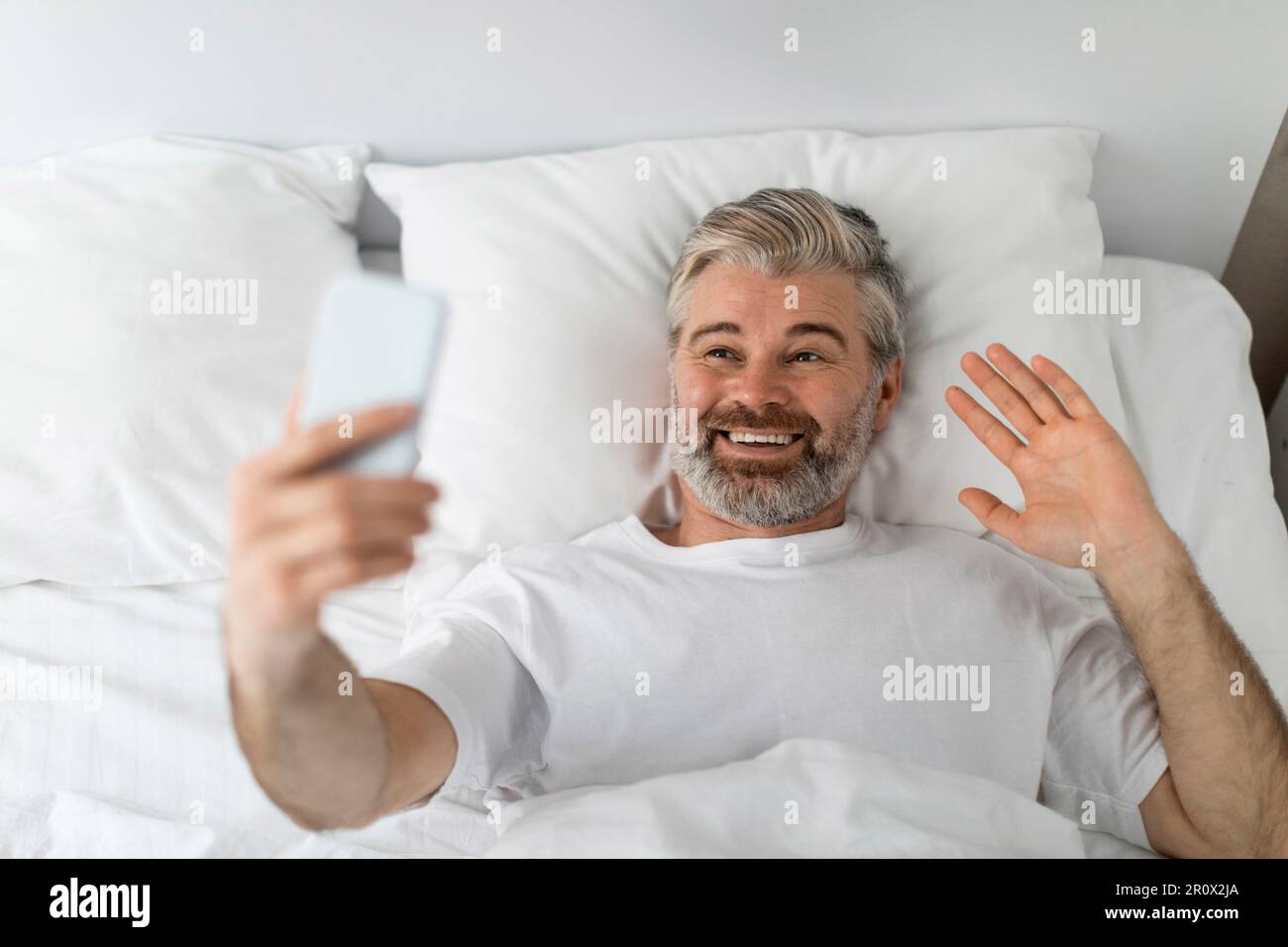 Draufsicht eines glücklichen Mannes, der im Bett telefoniert Stockfoto