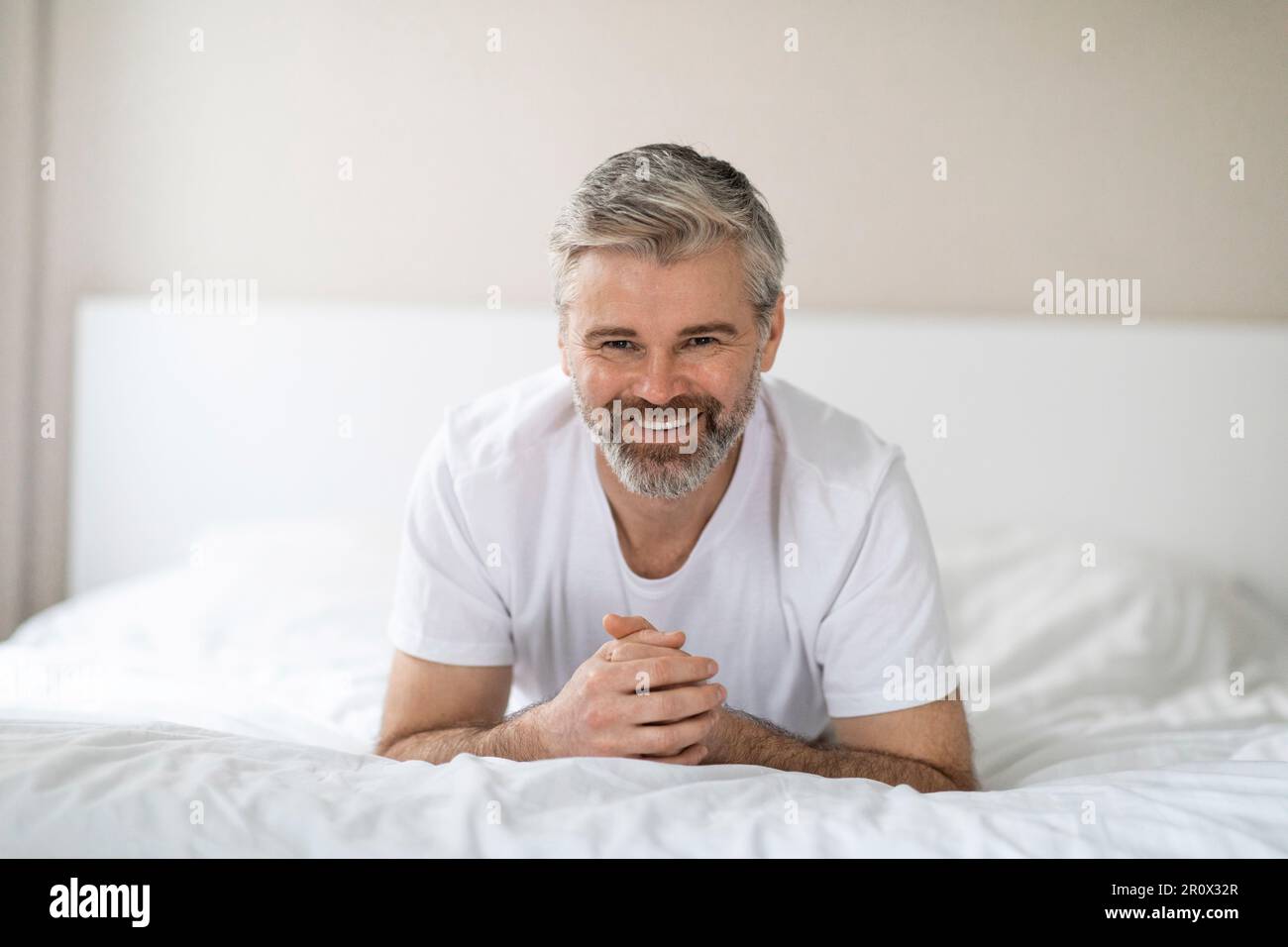 Porträt eines glücklichen Mannes mittleren Alters, der lächelnd im Bett liegt Stockfoto