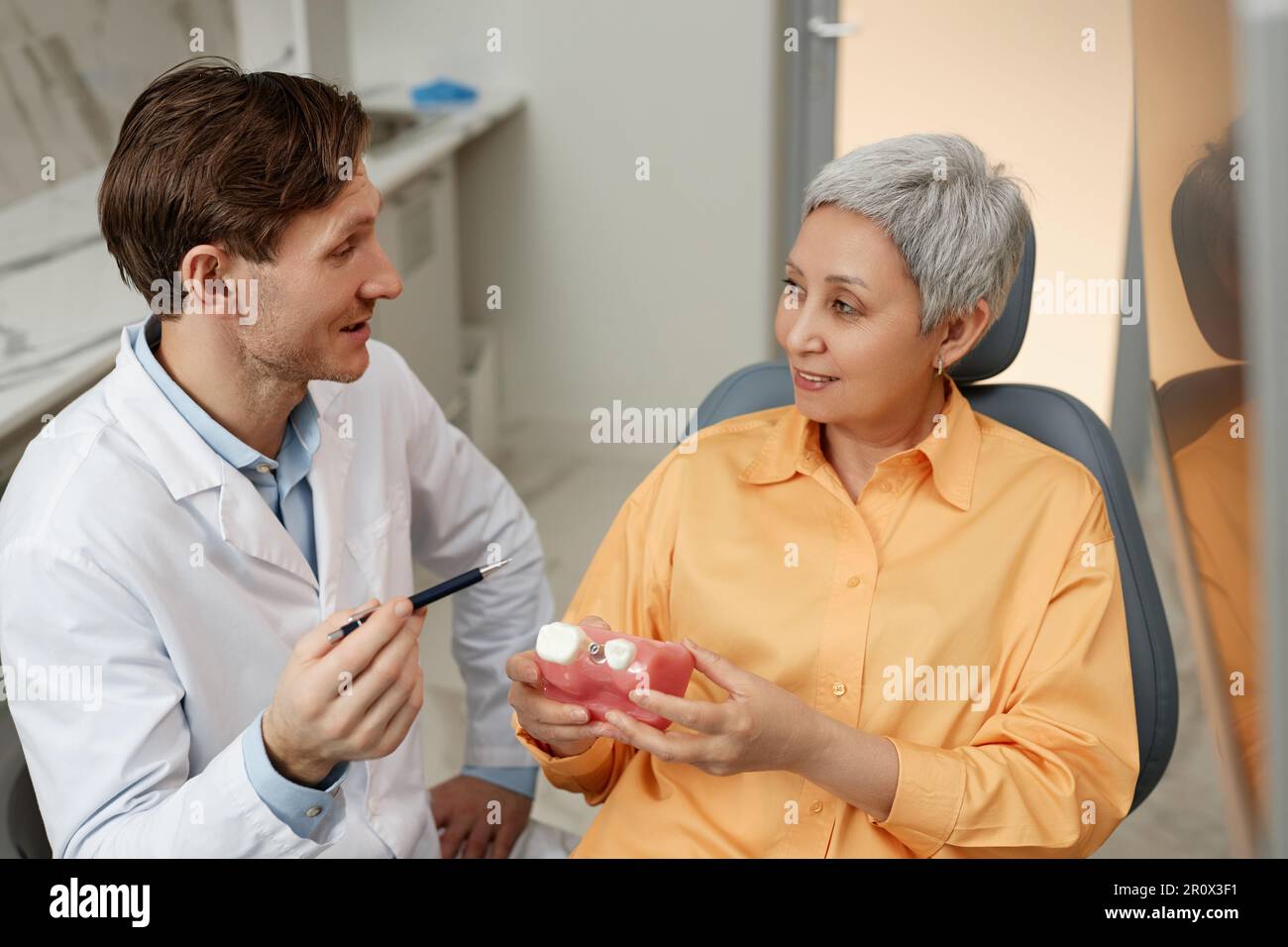 Seitenbild eines lächelnden männlichen Zahnarztes, der mit einer leitenden Zahnklinikerin während der Zahnimplantationsberatung spricht Stockfoto