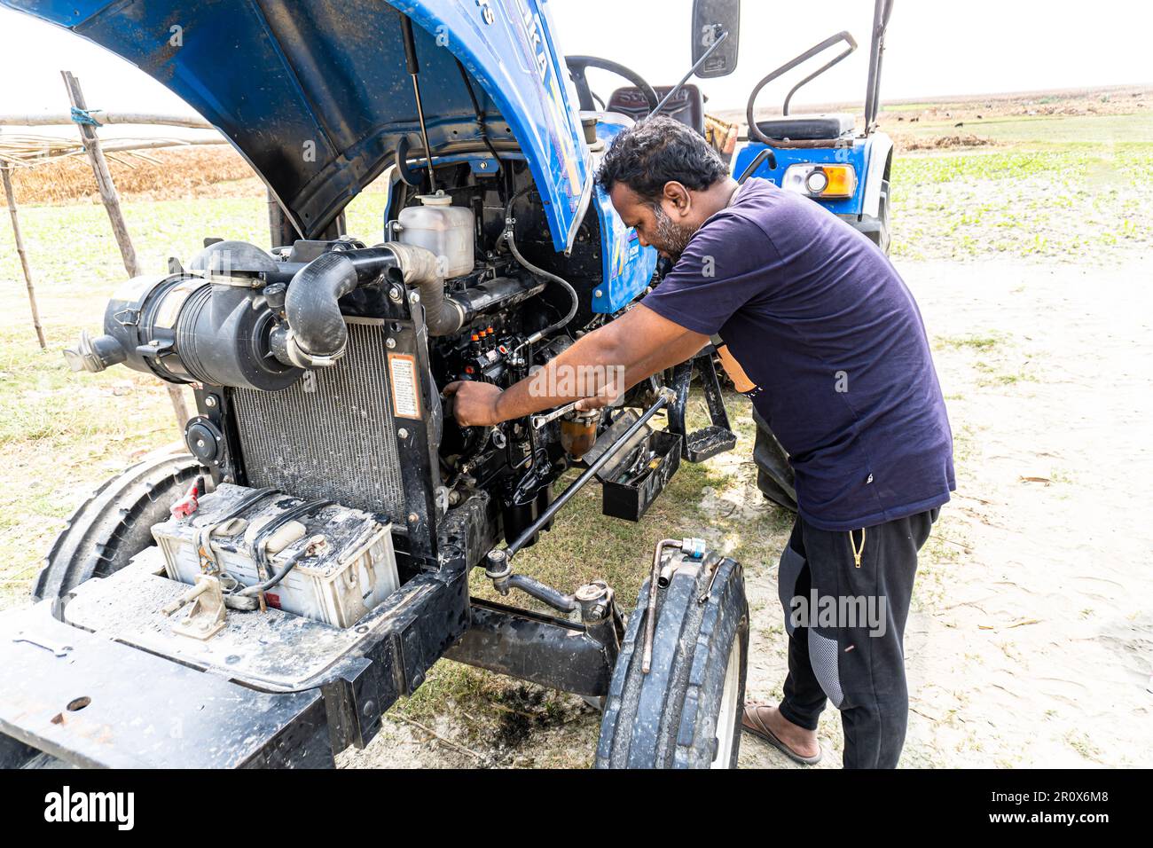 Landwirtschaftliche Technologie bei Sonnenuntergang reparieren. Öffnen Sie die Motorhaube des Traktors, den Motor. Bauernmechaniker, der den Motor eines blauen Traktors repariert Stockfoto