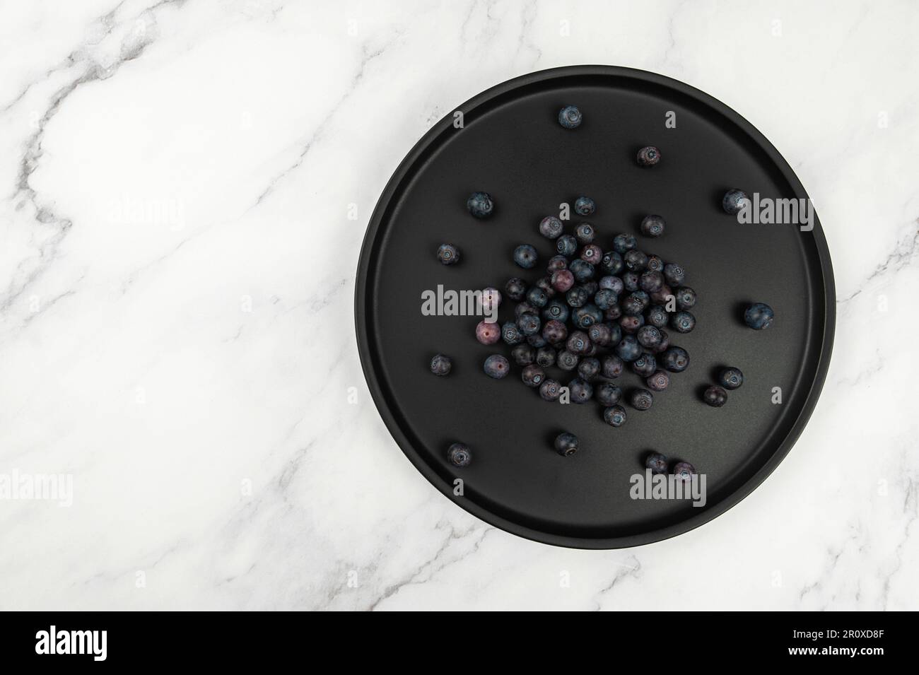 Draufsicht auf schwarzes Schild auf weißem Marmorhintergrund. Blaubeeren flach liegend, Kopierraum. Stockfoto