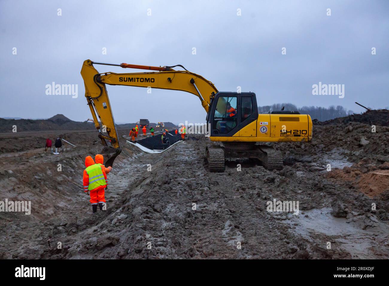 USt-Luga, Oblast Leningrad, Russland - 16. November 2021: Arbeiter machen Straßengräben mit Bagger. Bodenarbeiten an regnerischen Tagen Stockfoto