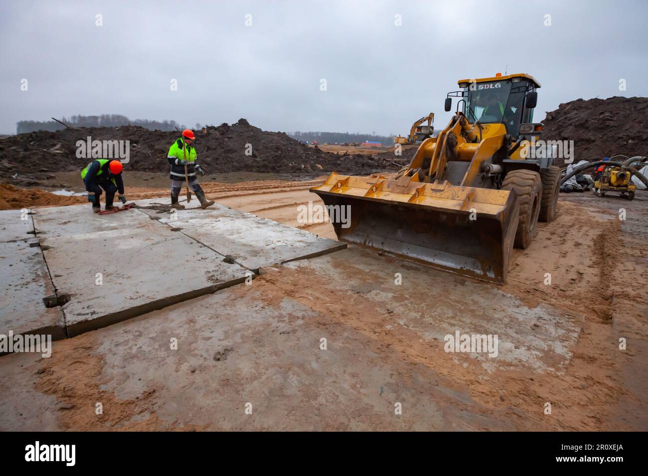 USt-Luga, Oblast Leningrad, Russland - 16. November 2021: Straßenbau. Arbeiter und Betonplatten mit Bulldozer auf Sanduntergrund aufstellen Stockfoto