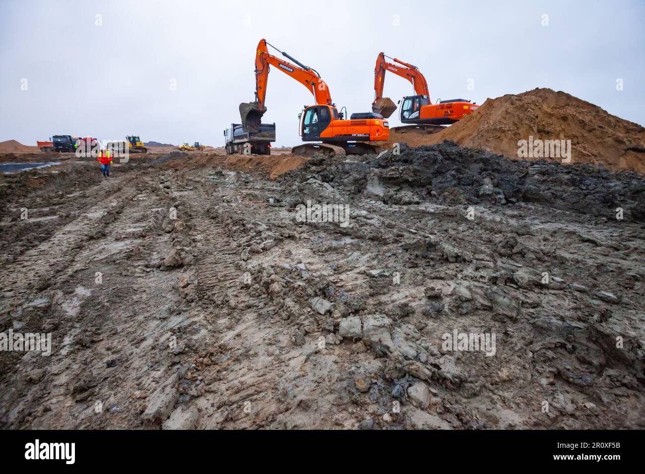 USt-Luga, Oblast Leningrad, Russland - 16. November 2021: Bagger Doosan und Hitachi auf der Baustelle. Ein Haufen Erde rechts. Regnerischer Tag, schlammige Roa Stockfoto