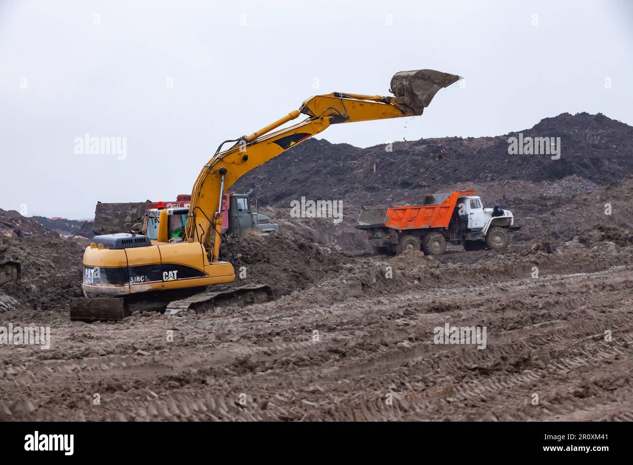 USt-Luga, Oblast Leningrad, Russland - 16. November 2021: Baustelle bei Regen. Bagger und Kipplaster bewegen sich auf dem Boden. Stockfoto