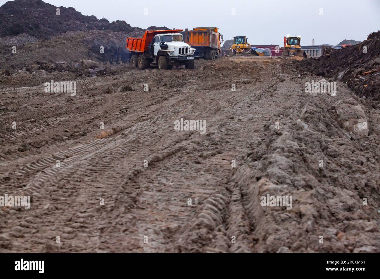 USt-Luga, Oblast Leningrad, Russland - 16. November 2021: Schmutzige Landstraße der Baustelle. Maschinen im Fokus. Stockfoto