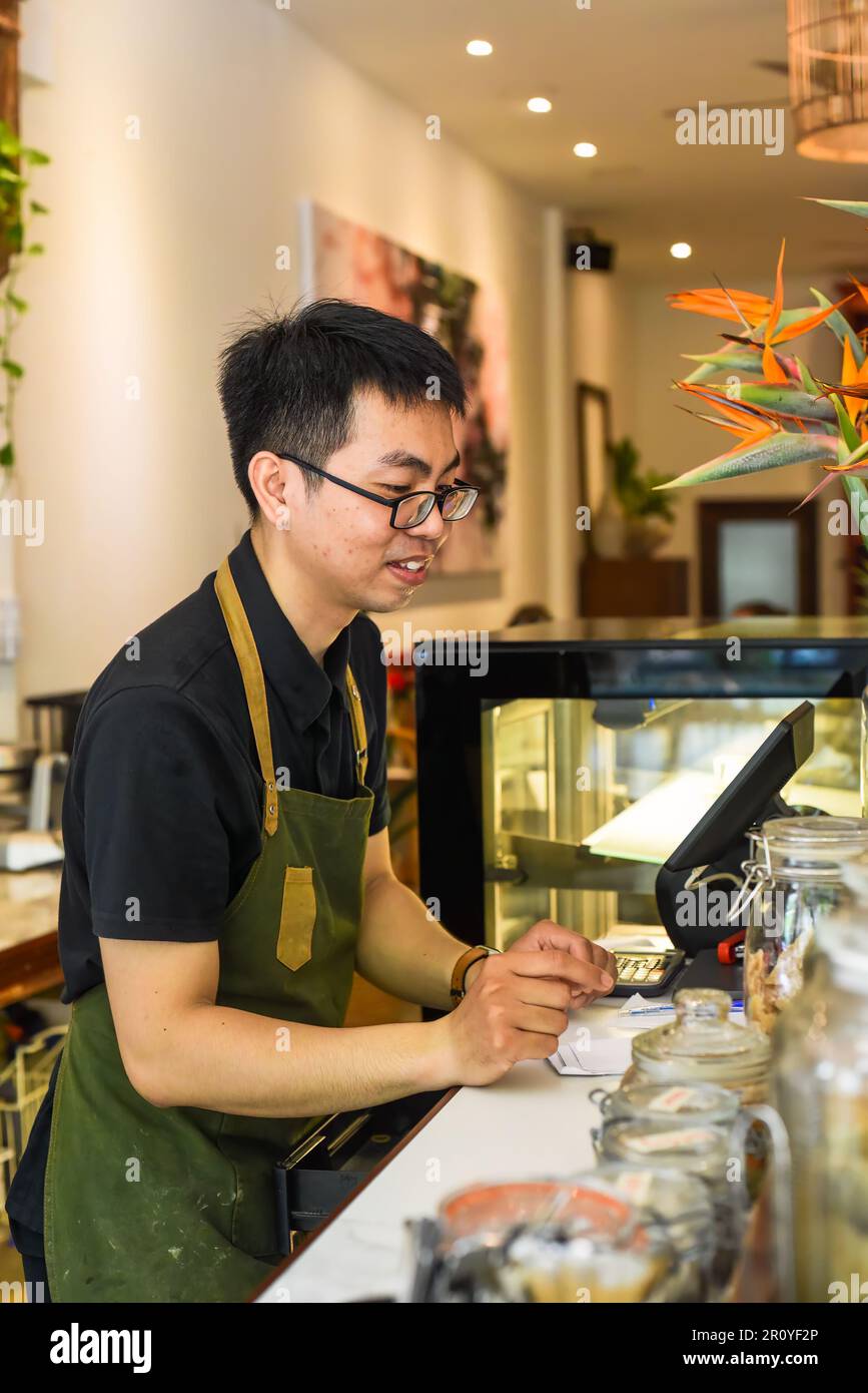 Vietnamesischer Kellner, der an der Theke arbeitet, mit einem Automaten in einem Café Stockfoto