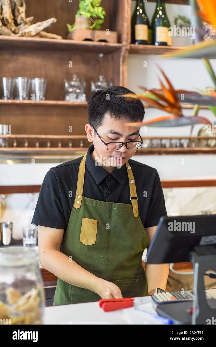 Vietnamesischer Kellner, der an der Theke arbeitet, mit einem Automaten in einem Café Stockfoto