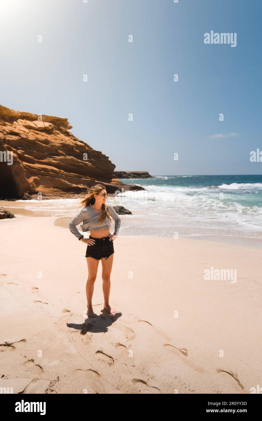 Eine junge, fit aussehende weiße Frau, die während ihres Sommerurlaubs am Playa de los Ojos auf der Kanarischen Insel Fuerteventura auf das Meer blickt. Stockfoto