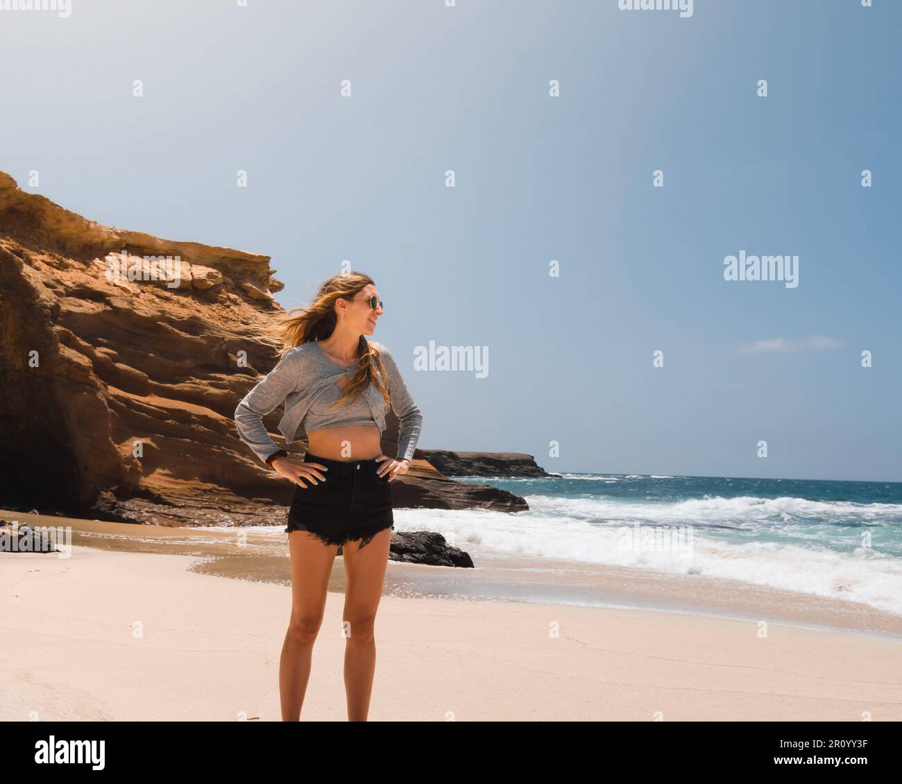 Die junge weiße Frau lächelt und schaut während ihres Sommerurlaubs am Playa de los Ojos auf der Kanarischen Insel Fuerteventura auf das Meer. Stockfoto