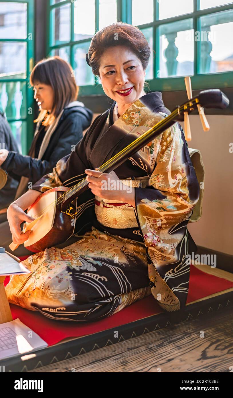 nagasaki, kyushu - 14 2022. dez.: Schammachtes Instrument, Demonstration mit Touristen durch eine japanische Frau im Kimono, die in einer traditionellen Seiza-Pose in t sitzt Stockfoto