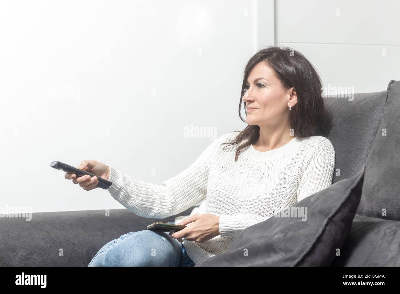Komfortabler Abend: Frau, die sich mit der Fernbedienung auf der weichen Couch entspannen kann Stockfoto