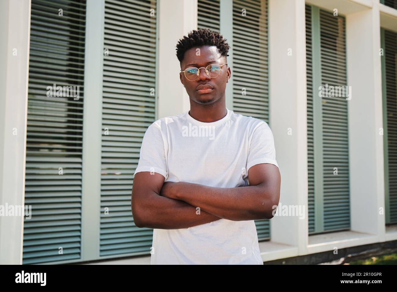 Porträt eines jungen afroamerikanischen, selbstbewussten Mannes, der vor der Kamera steht, mit gekreuzten Armen. Ein hübscher Student posiert mit einer ruhigen, nachdenklichen Einstellung auf dem Universitätscampus. Hochwertiges Foto Stockfoto
