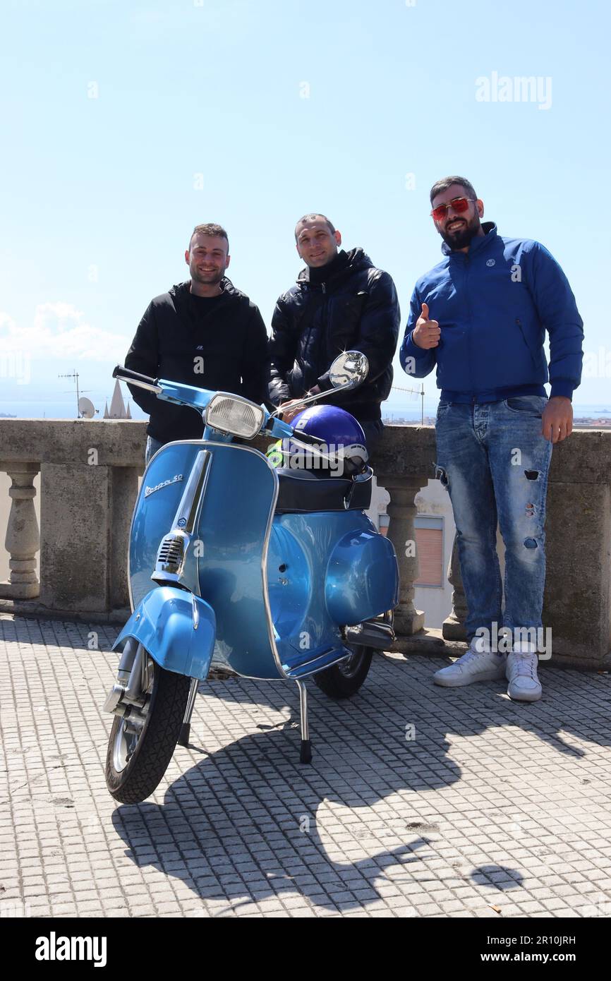 Drei junge Männer aus Messina stehen neben einer vollständig restaurierten Vespa 50s, entspannen sich auf ihren Motorrollern und essen in einem lokalen Barrestaurant. Stockfoto