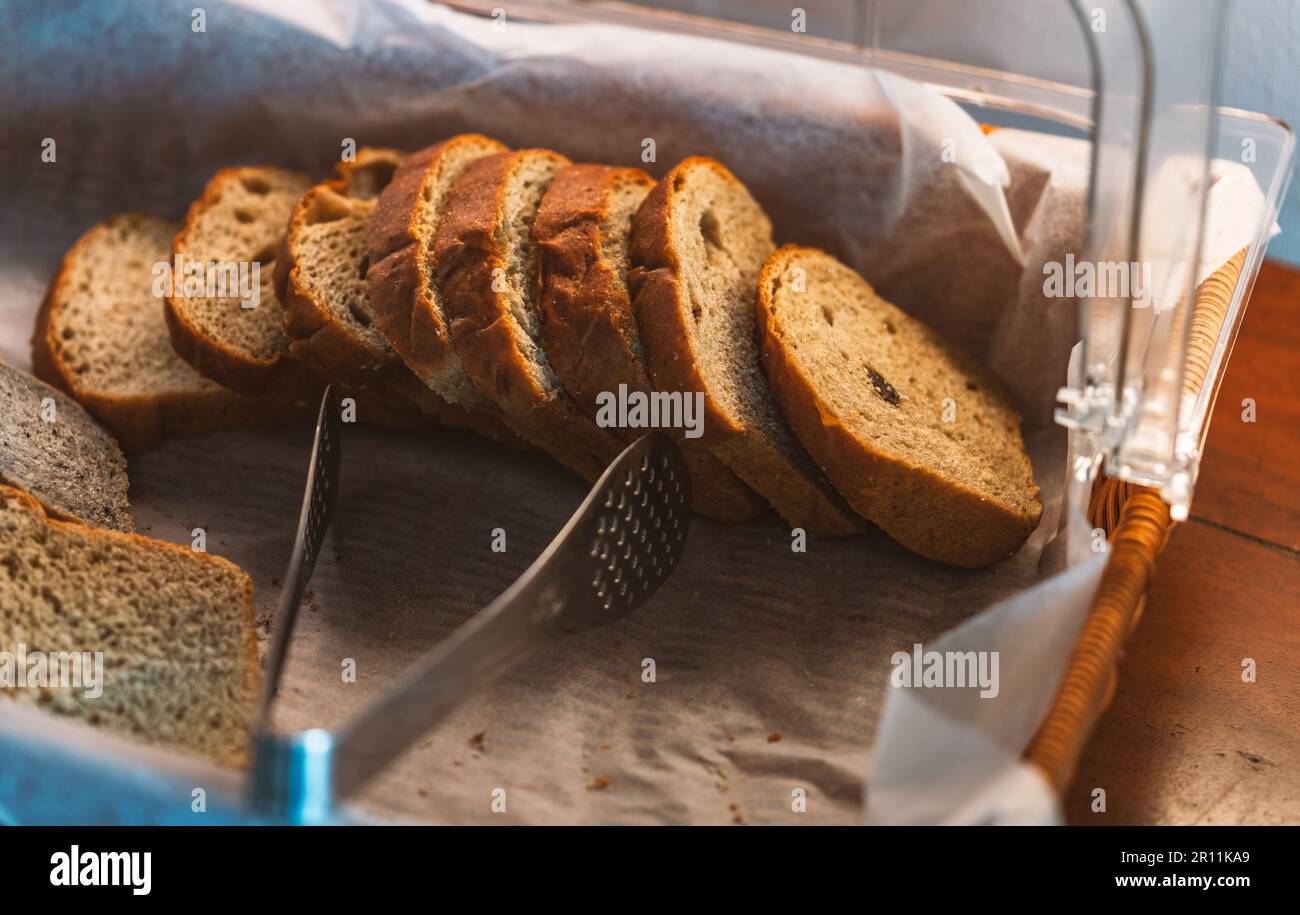 In einem Korb auf einem dunkelbraunen rustikalen Holztisch geschnittenes Vollkorbbrot, Tageslicht durch das Fenster. Stockfoto