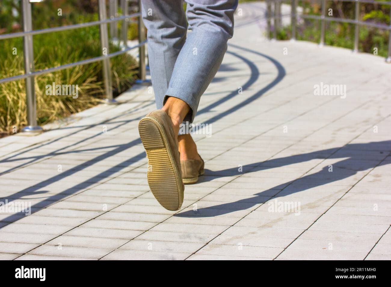 Die Füße des Fußgängers Geschäftsmann. Ein Mann in grauen Hosen, braune Schuhe, der an sonnigen Tagen auf der großen Straße spaziert. Lifestyle-Konzept für Geschäfts- und Urlaubsreisen. Contrasti Stockfoto