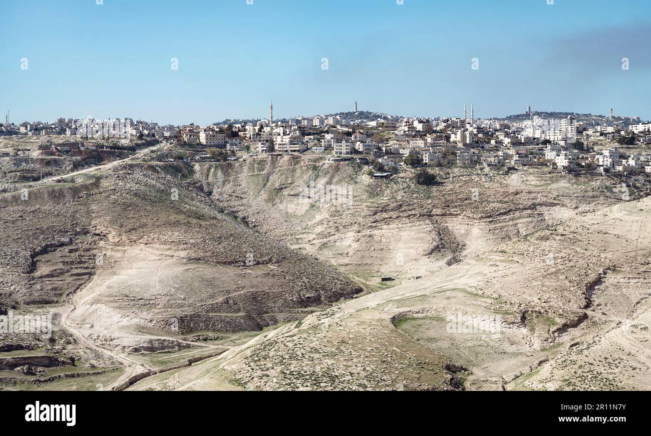 Die alte palästinensische Stadt al-Azariya befindet sich vor den Türmen von Ost-Jerusalem und hinter kargen Wüstenhügeln mit blauem Hintergrund Stockfoto