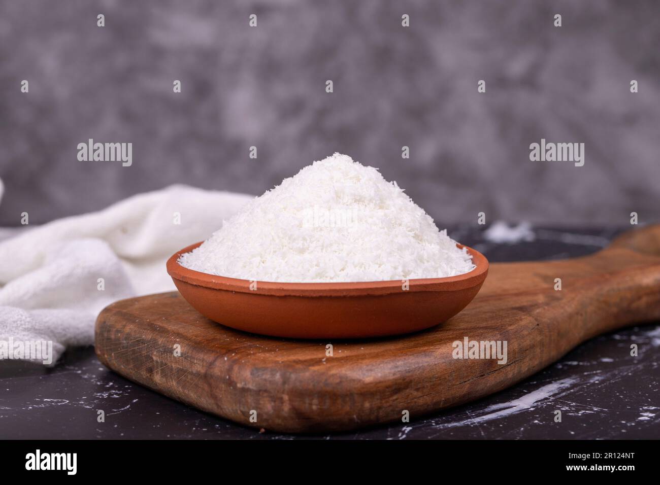Kokosnusspulver. Gemahlene Kokosflocken auf dunklem Hintergrund. Erdschüssel mit getrockneter Kokosnuss Stockfoto
