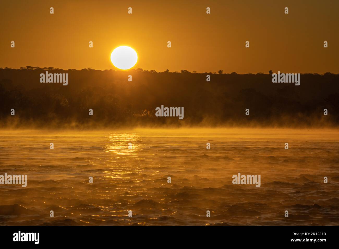 Sonnenaufgang über dem Sambesi-Fluss, die Wasseroberfläche leuchtet in leuchtenden orangefarbenen Farben auf, Nebel steigt aus dem Wasser auf. Sambesi, Simbabwe, Afrika Stockfoto