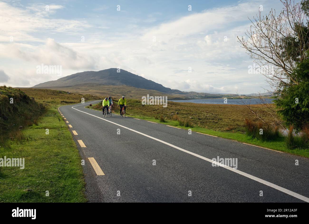 Gruppe von Personen, die durch die malerische Natur am lough inagh mit Bergen im Hintergrund im Connemara National Park in der Grafschaft Galway, Irland radeln Stockfoto