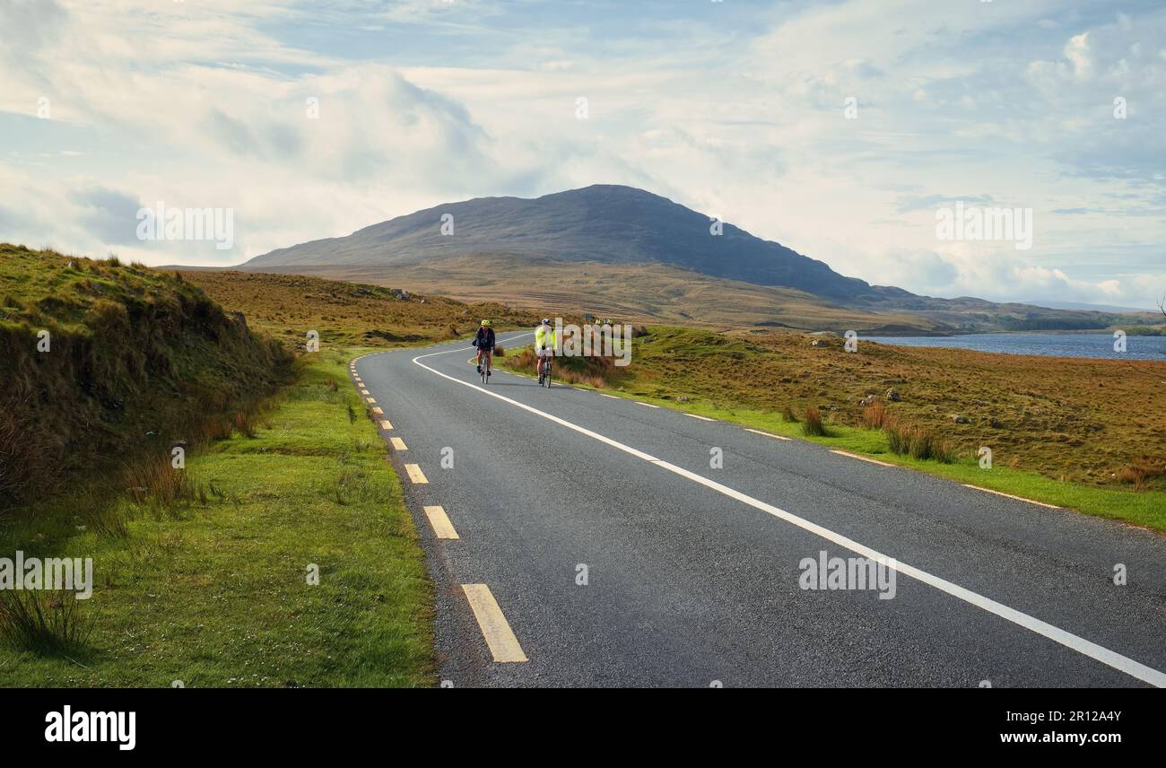 Gruppe von Personen, die durch die malerische Natur am lough inagh mit Bergen im Hintergrund im Connemara National Park in der Grafschaft Galway, Irland radeln Stockfoto