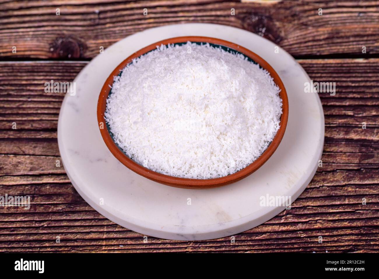 Gemahlene Kokosflocken auf Holzhintergrund. Kokosspäne in Tonschüssel Stockfoto