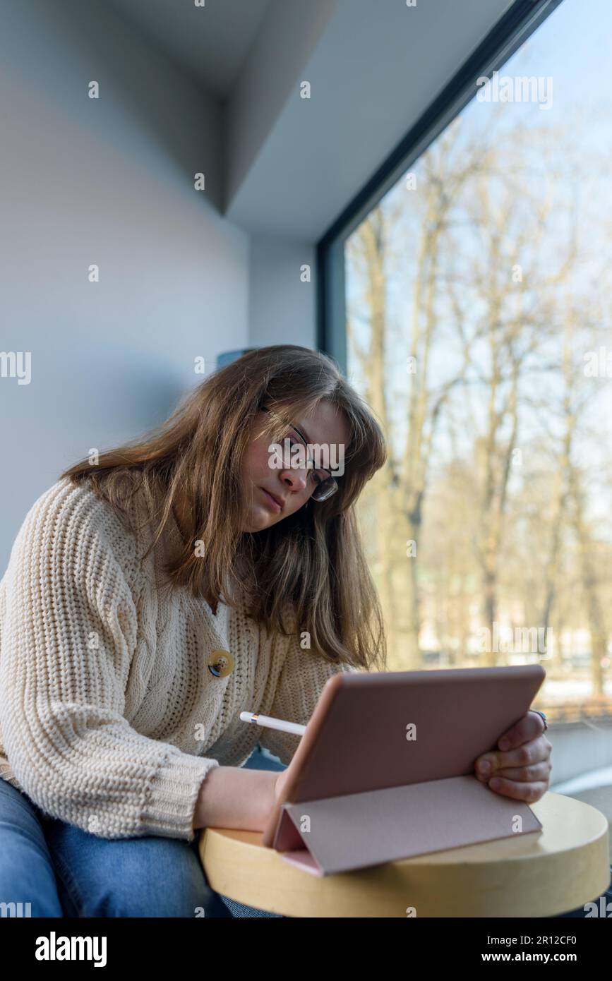 Junge Frau in Strickpullover und Brille zeichnen oder arbeiten auf Tablet-pc Stockfoto