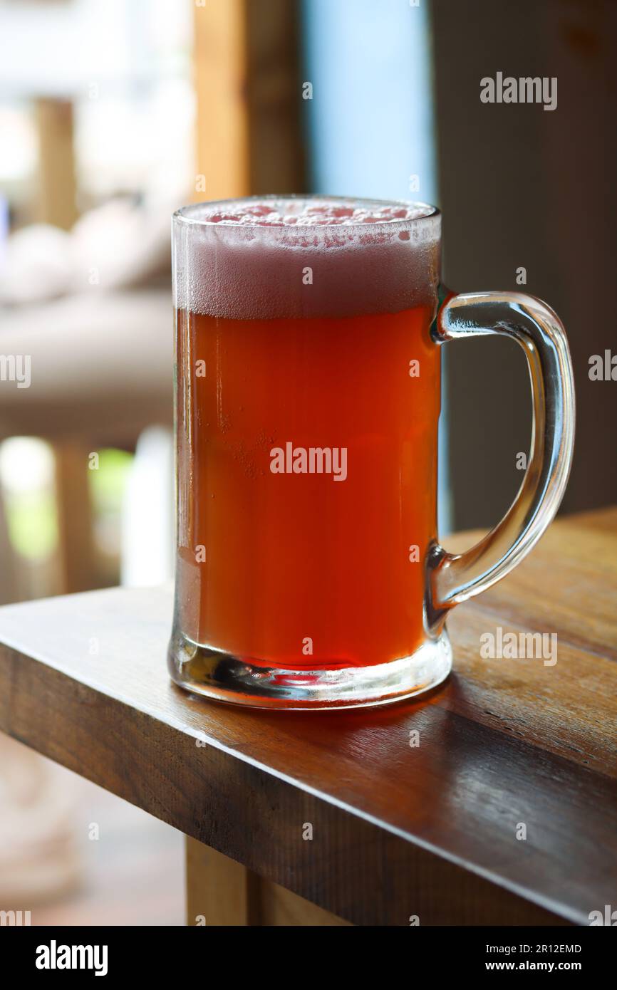 Eine Tasse kaltes, leichtes Bier mit Granatapfelsaft und Schaum auf dem Restauranttisch. Reale Fotografie in einem Restaurant, sonniger Tag, leichtes kaltes Bier auf t Stockfoto