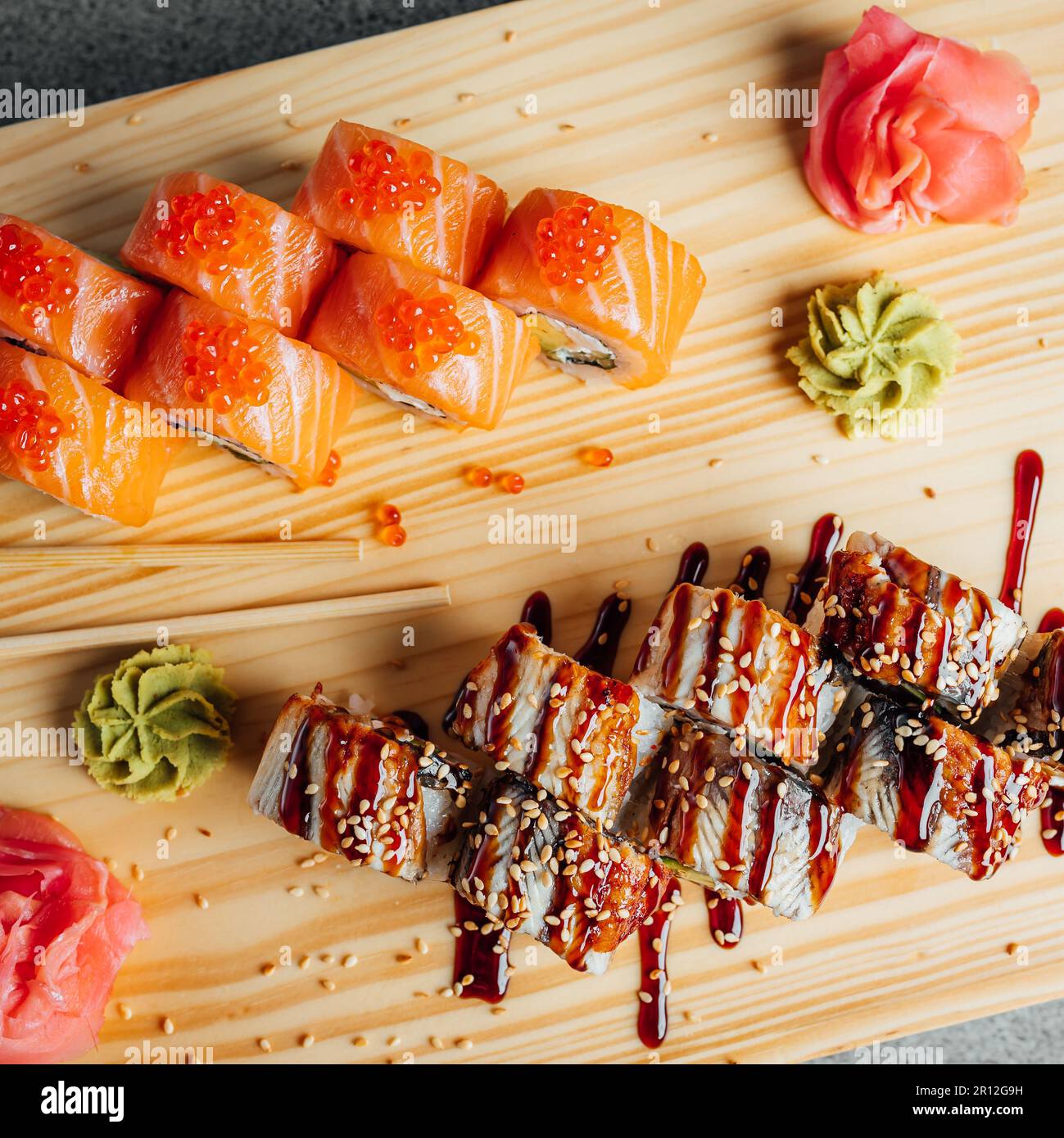 Eine Auswahl an frisch zubereiteten Sushi-Brötchen, einschließlich Sashimi, die auf einem rustikalen Holzbrett angeordnet sind und zum Genießen bereitstehen Stockfoto
