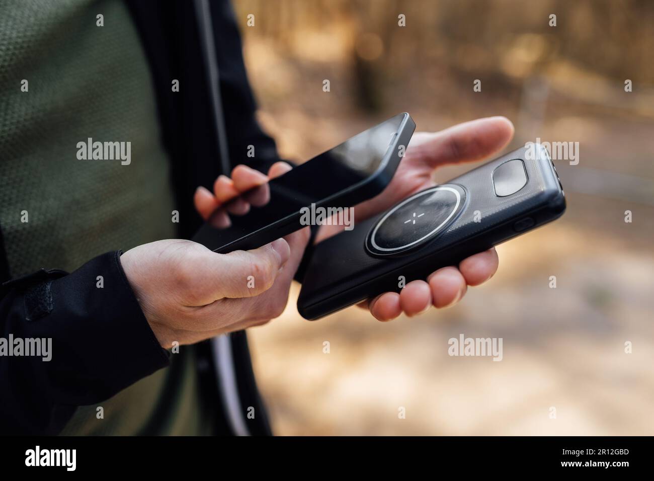 Nahaufnahme der Hände einer Person, die ein Smartphone und ein schnurloses Telefonladegerät hält Stockfoto