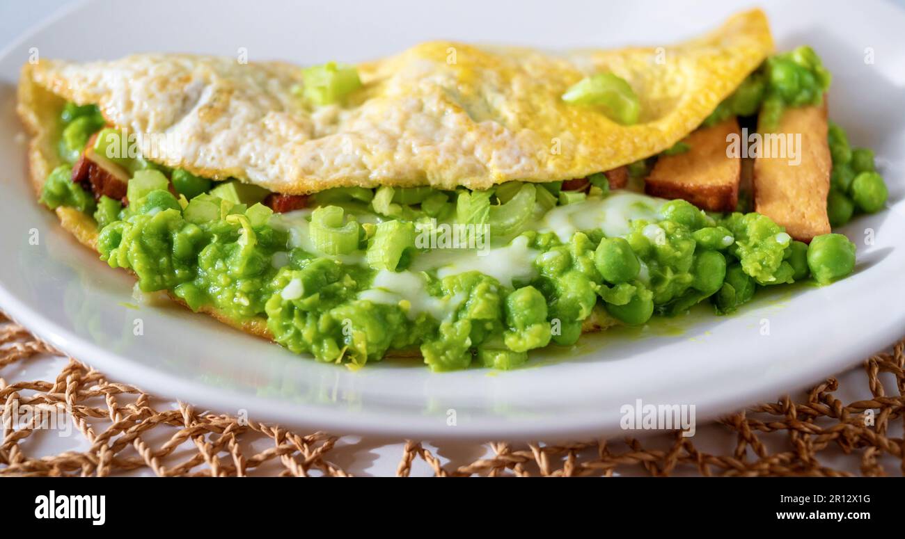 Eieromelette mit pürierter, frischer grüner Erbse, Selleriestangen und geräuchertem Tofu auf weißem Teller auf Bambuspad, Nahaufnahme. Stockfoto