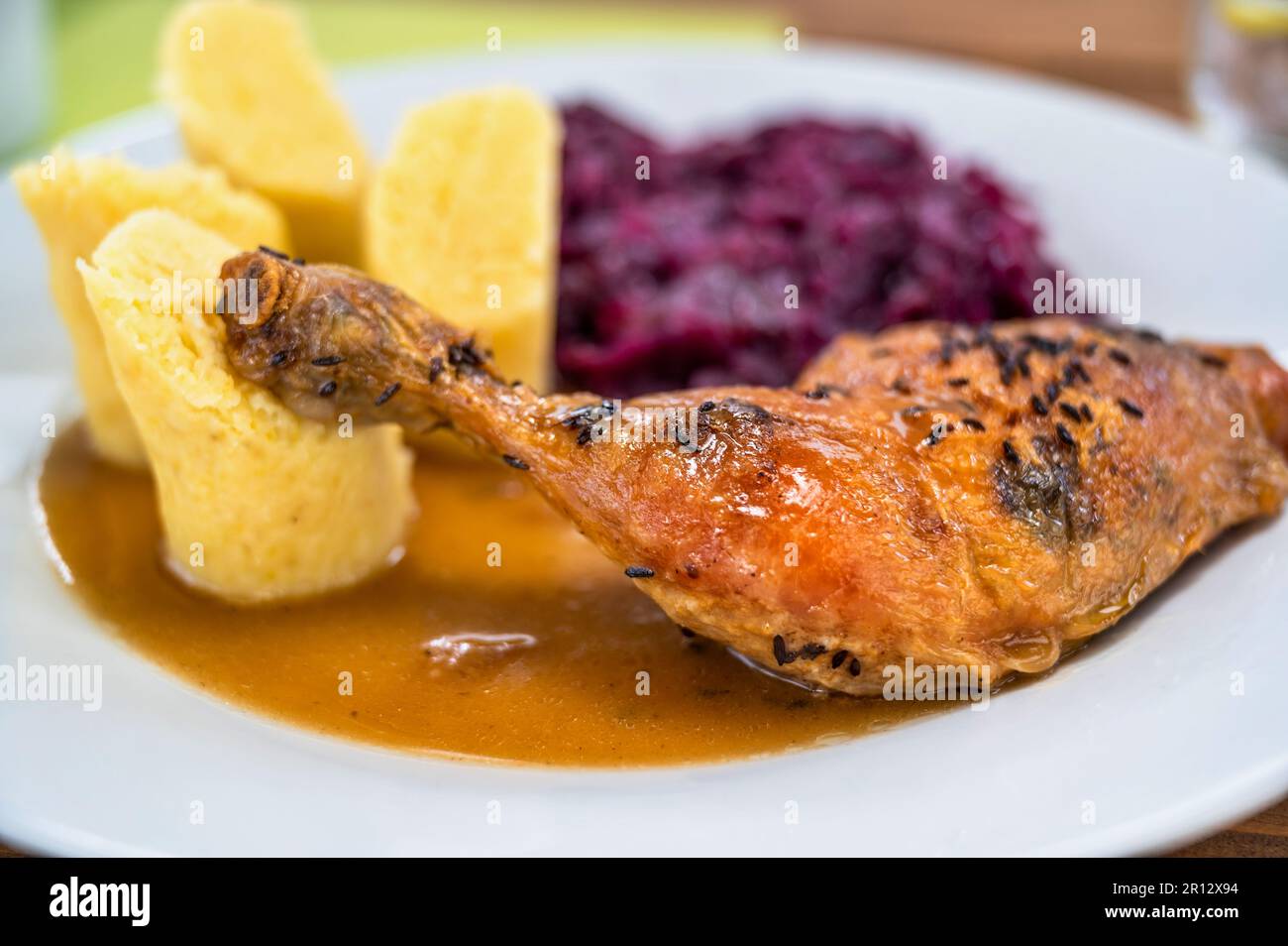 Gebratenes Hähnchenschenkel, gedünsteter Rotkohl und flauschige Kartoffelklöße auf weißem Teller, Nahaufnahme. Stockfoto