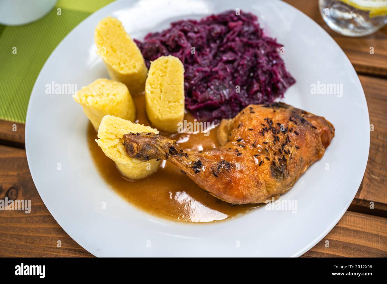 Gebackenes Hähnchen am Schenkel, gedünsteter Rotkohl und flauschige Kartoffelklöße auf weißem Teller, Nahaufnahme. Stockfoto