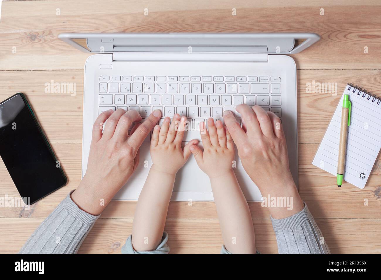 Die Hände einer Mutter und ihres einjährigen Kindes sind auf einer Laptop-Tastatur sichtbar. Stockfoto