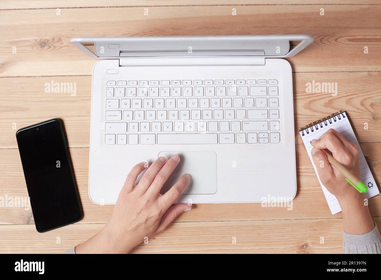 Die Hände der Frau sind auf einer Laptop-Tastatur sichtbar und in einem Notebook zu schreiben. Stockfoto