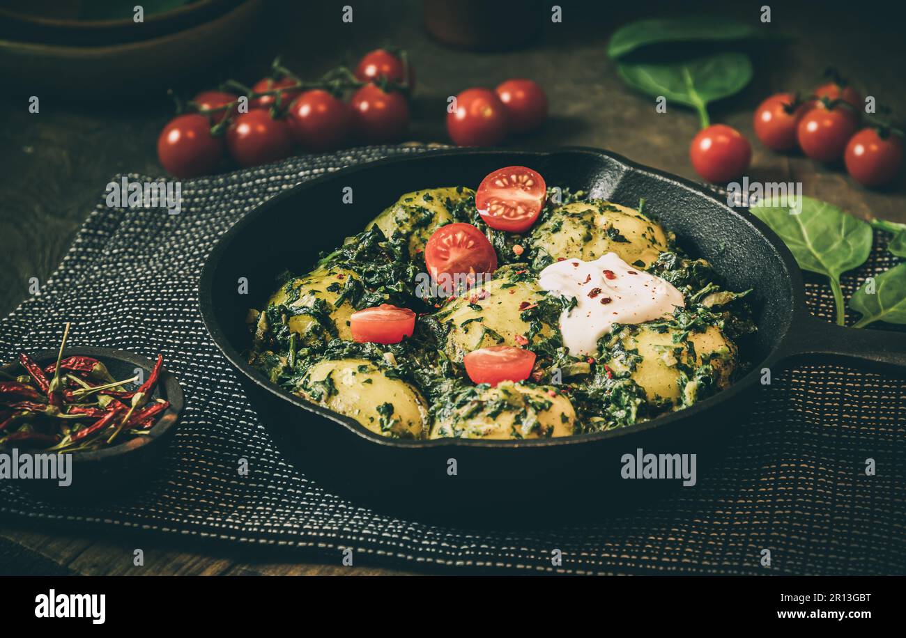 Kartoffelpfanne mit Spinat, vegetarische Küche, auf einem dunklen rustikalen Tisch Stockfoto