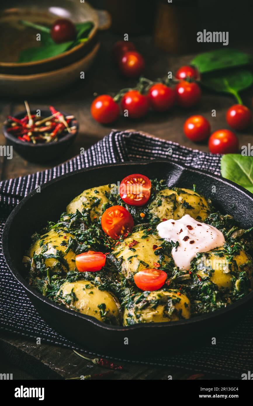 Kartoffelpfanne mit Spinat, vegetarische Küche, auf einem dunklen rustikalen Tisch, vertikal Stockfoto