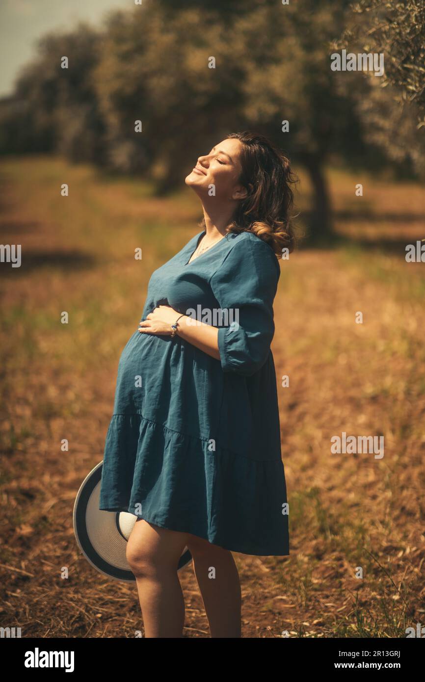 Eine schwangere Frau mit einem blauen weißen Hut in einem Olivenfeld mit geringer Schärfentiefe. Stockfoto