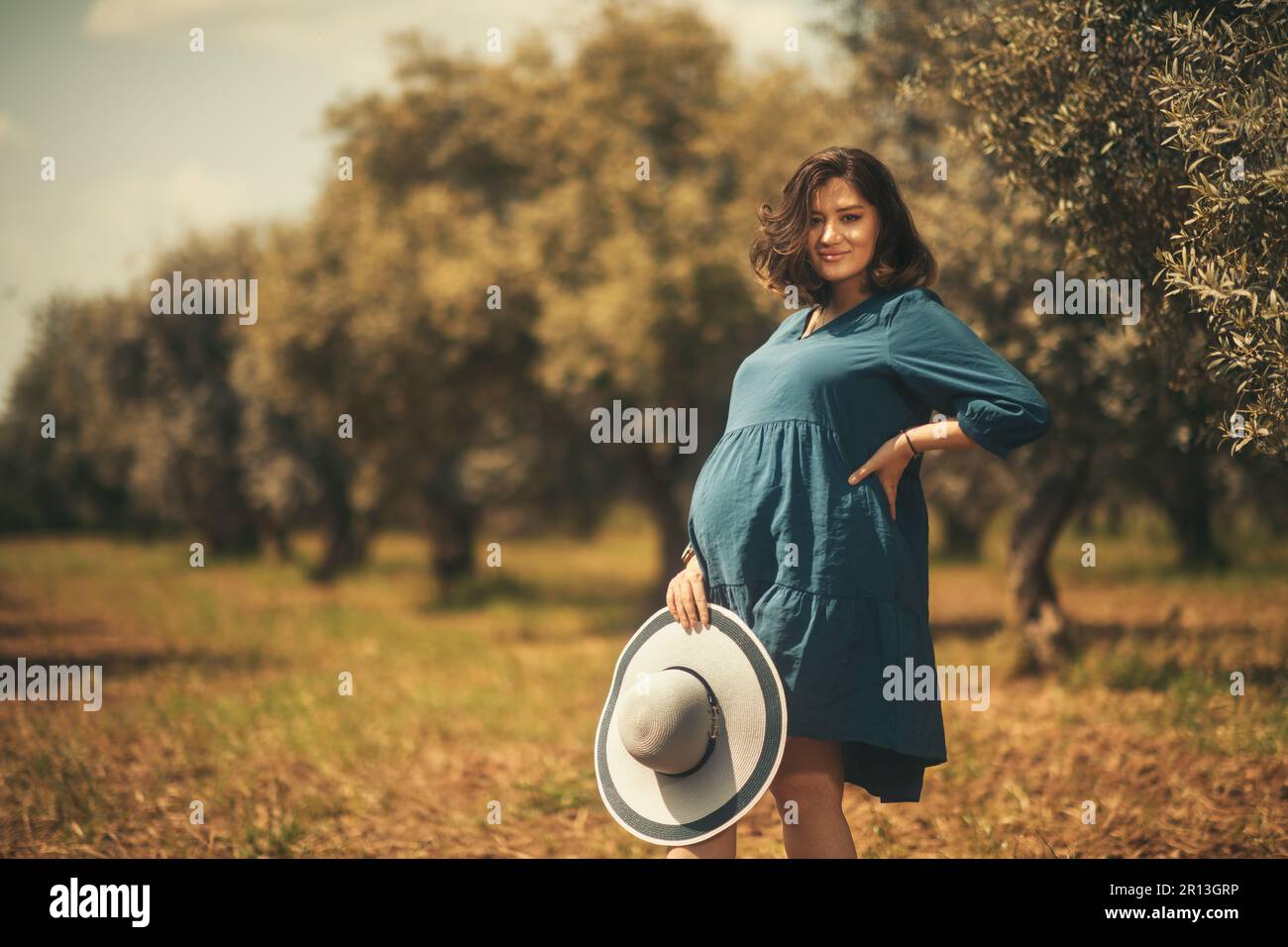 Eine schwangere Frau mit einem blauen weißen Hut in einem Olivenfeld mit geringer Schärfentiefe. Stockfoto
