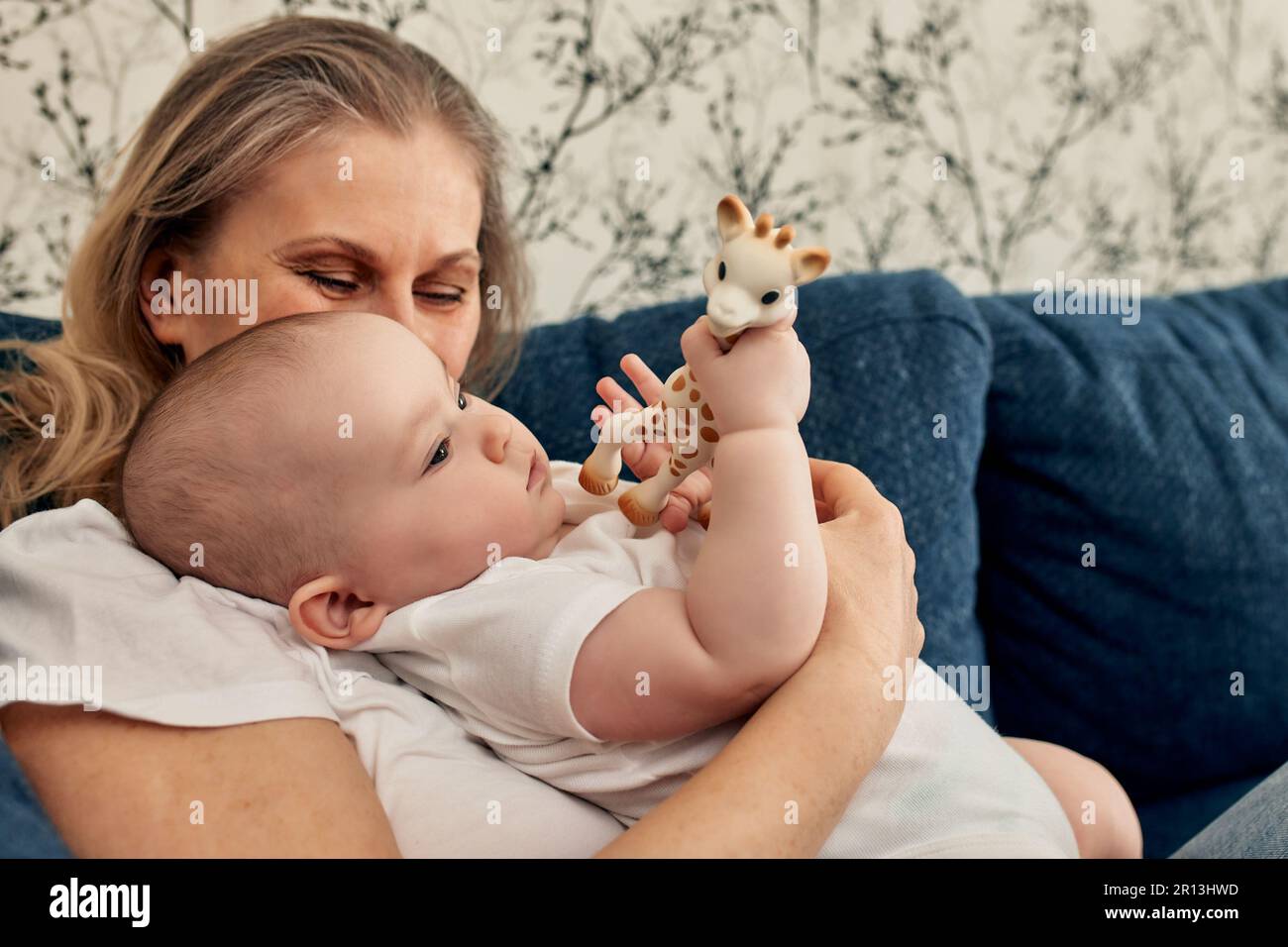 Eine liebevolle Mutter hält ihr Kind in den Armen, die mit einer Giraffe spielt. Mütterliche Liebe, Lernen und Aktivität eines Neugeborenen im Spiel Stockfoto