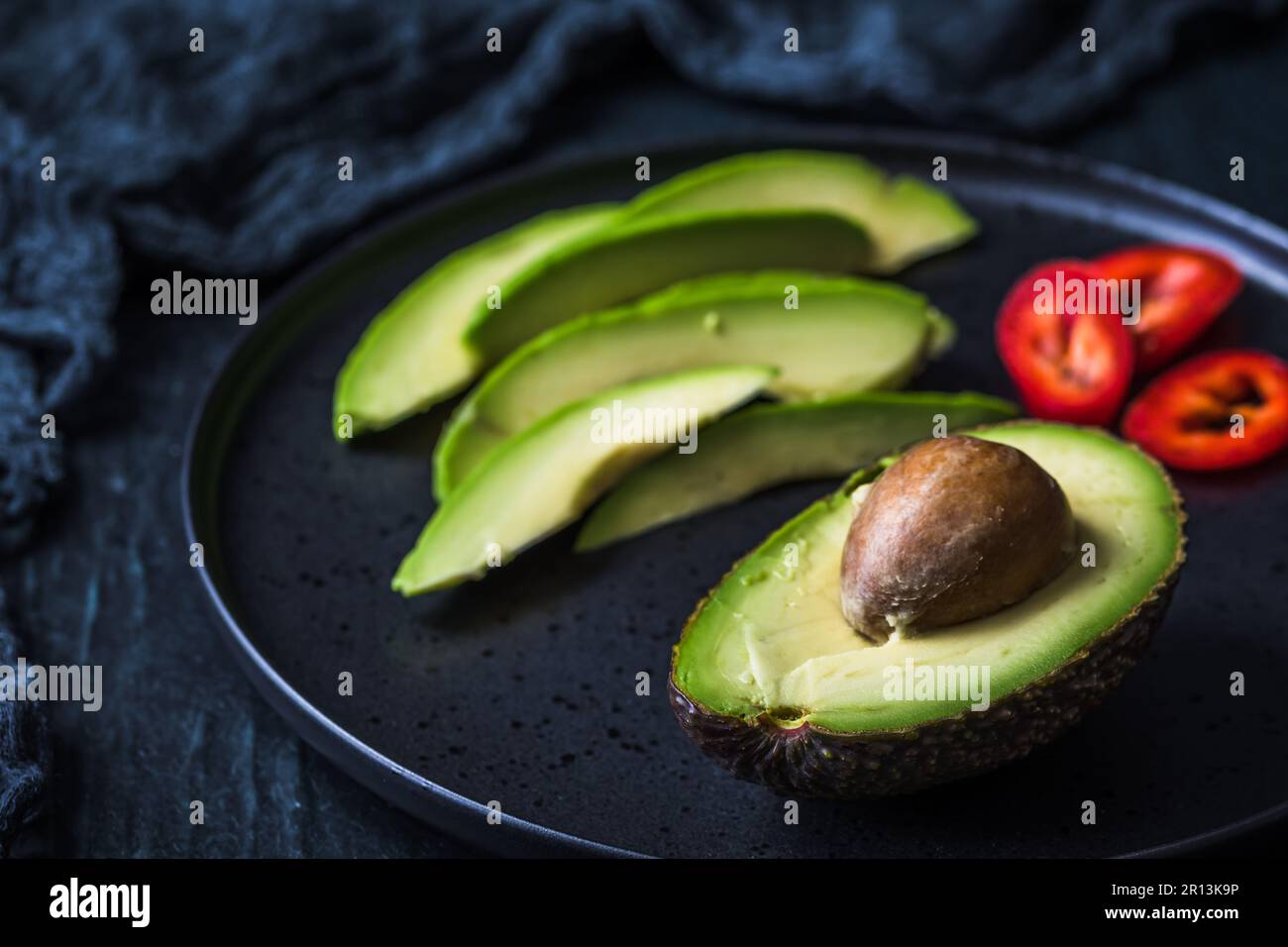 Halber Avocado mit Grube und Avocado-Scheiben auf schwarzem Teller Stockfoto