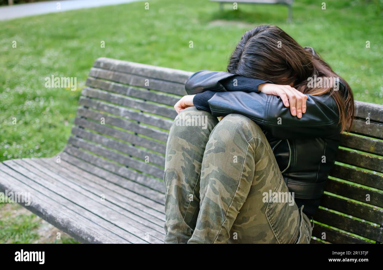 Junge Frau traurig und depressiv auf der Parkbank mit Armen und Kopf auf Knien Stockfoto